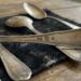Old tarnished silver spoons resting on a dark cloth on a rustic wooden table, displaying 925 hallmarks.