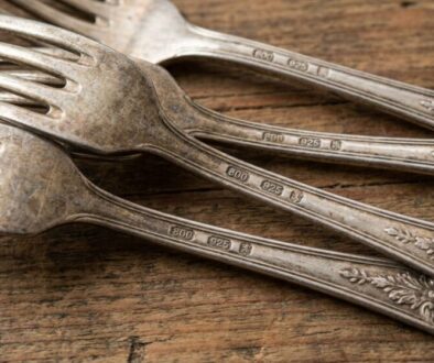 Group of tarnished metal forks with decorative handles laid on a rustic wooden surface, showing wear and patina.