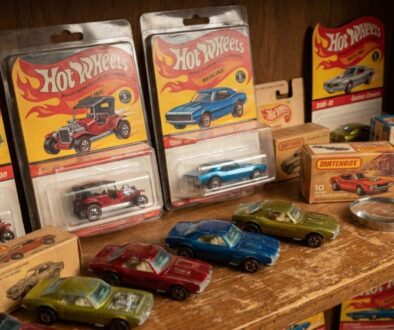 Row of vintage Hot Wheels die-cast cars in red, blue, and green on a wooden shelf with packaging visible behind them.