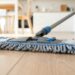 Close-up of a flat mop cleaning a wooden floor in a bright kitchen.