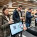 Shoppers at a supermarket checkout using mobile QR payments at a touchscreen terminal.