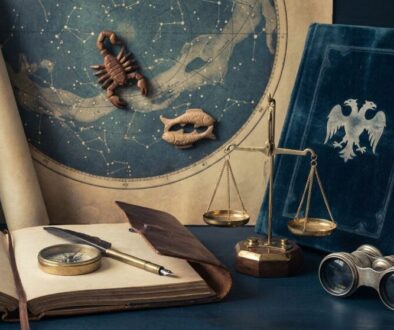 Vintage explorer’s desk with a star map, balance scales, magnifying glass, compass, and antique notebook on a dark wooden surface.