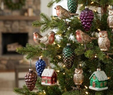 Christmas tree with metal bird, owl, pinecone, berry ornaments and tiny red and green house decorations under warm lights