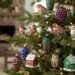 Christmas tree with metal bird, owl, pinecone, berry ornaments and tiny red and green house decorations under warm lights