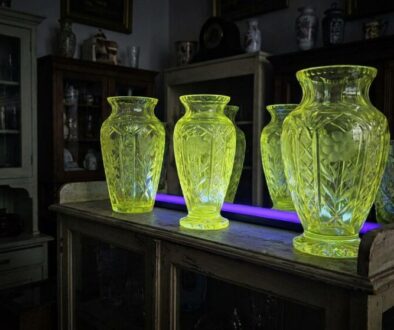 Three lime-green cut-glass vases sit on an old wooden cabinet in a dim antique room.