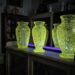 Three lime-green cut-glass vases sit on an old wooden cabinet in a dim antique room.