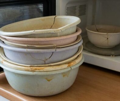 Stack of cracked pastel ceramic bowls piled on a wooden kitchen counter beside a microwave.