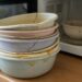 Stack of cracked pastel ceramic bowls piled on a wooden kitchen counter beside a microwave.