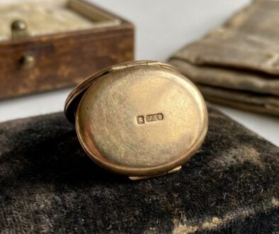 Antique gold pocket watch resting on a black velvet cushion, with a worn wooden box in the blurred background.