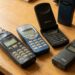 Five early mobile phones on a wooden table, including Nokia models and a Motorola flip phone.