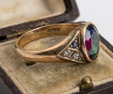 Antique gold ring with an oval multicolored gemstone in a worn velvet jewelry box