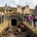 Tour group watches archaeologists excavate a shallow trench inside an ancient stone fortress.