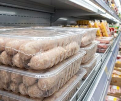 Stack of transparent plastic trays filled with raw sausages on a supermarket shelf in the refrigerated aisle