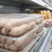 Stack of transparent plastic trays filled with raw sausages on a supermarket shelf in the refrigerated aisle