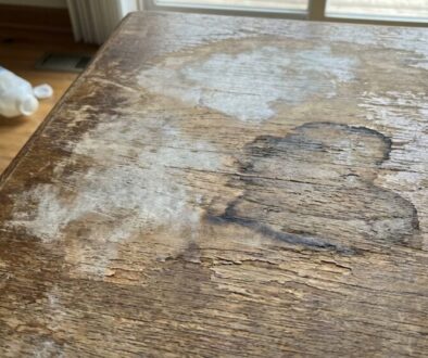 Close-up of a worn wooden table with peeling varnish and water stains, showing a rough, aged surface.