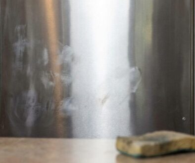Stainless steel kitchen appliance with smudges; a spray bottle and sponge sit on the counter in front of it.