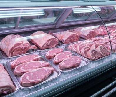 Assorted raw pork cuts arranged on metal trays in a refrigerated display case at a butcher shop.