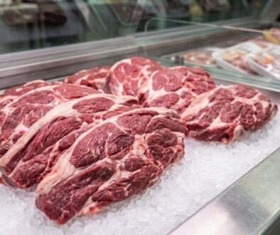 Several raw beef ribeye steaks on crushed ice in a glass display case.