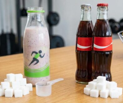 Berry smoothie in a bottle beside sugar cubes, a small scoop, and two cola bottles on a gym counter.