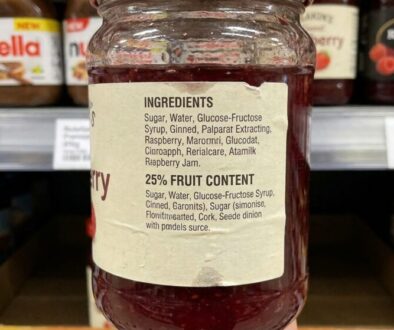 Jar of red fruit jam on a store shelf with a beige label listing ingredients and 25% fruit content in clear print.