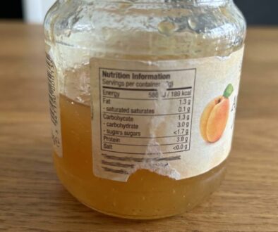 Jar of peach jam on a wooden table with the nutrition information label clearly visible on the front edge.