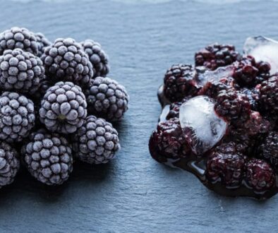 Piled frosted blackberries on a blue slate, with a light powdery frost coating each berry.