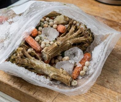 Open zip-top bag of frozen mixed vegetables on a wooden countertop, showing broccoli stems, carrot pieces, and peas with ice crystals visible inside the bag