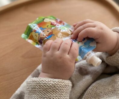 Baby's hands squeeze a colorful pouch of baby food on a wooden tray.