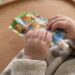 Baby's hands squeeze a colorful pouch of baby food on a wooden tray.