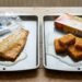 Two baking sheets on a wooden table—left with a raw fish fillet and drippings, right with breaded nuggets and an open box nearby.