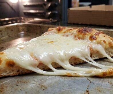 Slice of cheese pizza on a baking sheet with molten mozzarella stretching from the slice.