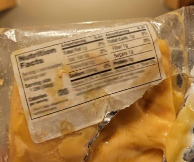 Foil-wrapped cheese slice with melted cheese oozing out and a partially visible nutrition label.