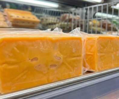 Blocks of orange cheddar cheese in clear plastic wrap on a supermarket dairy shelf