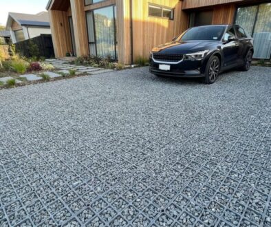 Black SUV parked on a geometric grid-paver driveway in front of a modern wooden house with minimalist landscaping on the left.