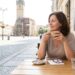 Woman sipping coffee at an outdoor cafe table on a cobblestone street with historic buildings in the background.