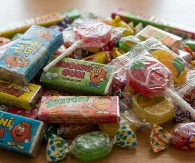 Pile of colorful candy wrappers and chewing gum boxes scattered on a wooden surface.