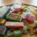 Pile of colorful candy wrappers and chewing gum boxes scattered on a wooden surface.