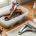 Rusty wrenches and gears soaking in a plastic tub of soapy water on a wooden workbench.