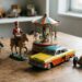 Collection of vintage tin toys on a wooden table: robot, horse-mounted soldier, carousel, yellow-and-red car, and a vintage race car with driver on display.