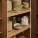 Wooden pantry shelves with glass jars of grains, a woven basket, and scattered bay leaves for a rustic display.