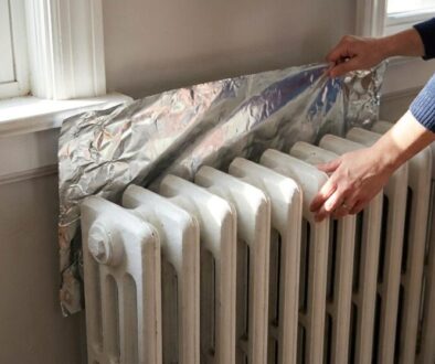 Person installing reflective foil behind a radiator by a window.