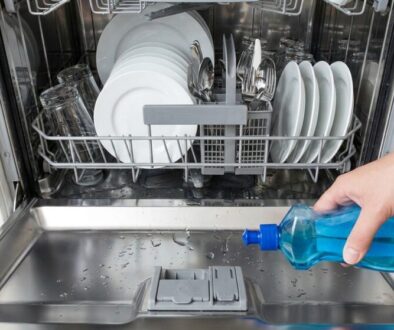 Person pouring blue dish soap into a dishwasher's open door for cleaning dishes