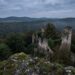 Ruined stone castle atop a mossy rocky outcrop overlooking a misty forest valley beneath a cloudy sky