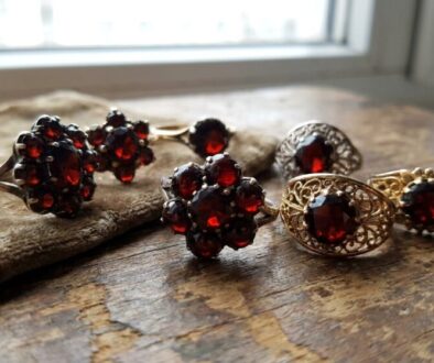 Set of vintage rings with dark red gems arranged on a rustic wooden surface near a window.