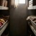 Rustic pantry with crates of produce: left crate filled with onions, right crate with potatoes, wicker baskets on shelves and sunlight from a small window![