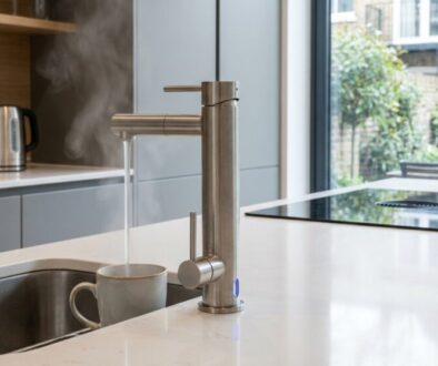Modern kitchen with a tall stainless steel faucet pouring water into a mug at a white island, kettle on the counter nearby.