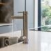 Modern kitchen with a tall stainless steel faucet pouring water into a mug at a white island, kettle on the counter nearby.