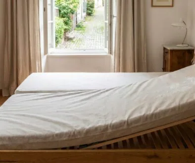 Bright bedroom with a wooden bed frame and an open window showing a stone path and greenery outside