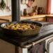 Cast iron skillet on a rustic stove filled with roasted potatoes and sausages, steaming in a cozy country kitchen.