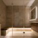 Modern beige-tiled bathroom with a glass walk-in shower, wooden vanity, a built-in bench, towels, and a potted plant on the counter.
